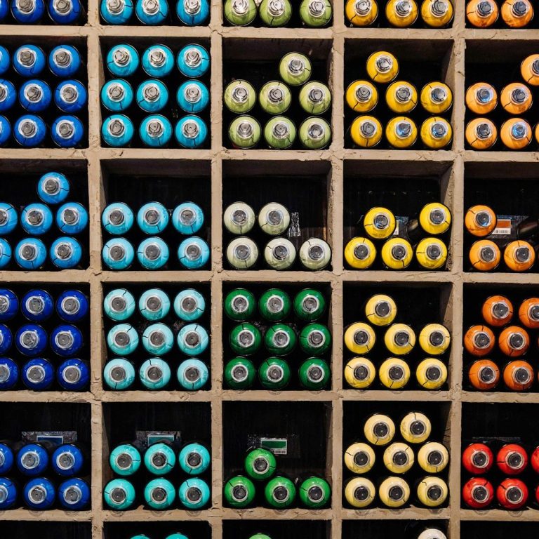 Farbenfrohe Lackflaschen in einem Holzkasten, ordentlich in Quadraten angeordnet.