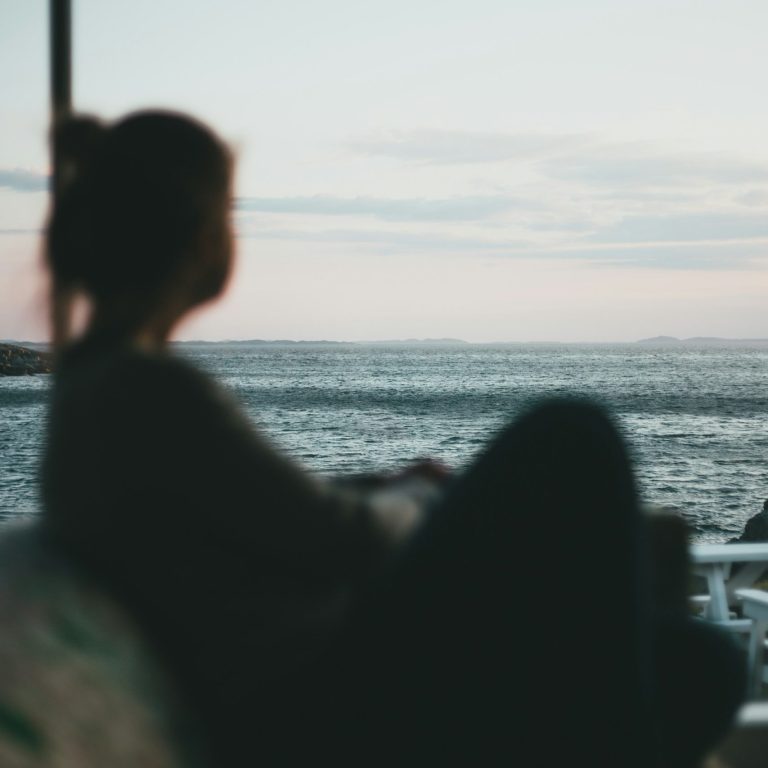 Frau schaut nachdenklich auf das Wasser und die Küstenlandschaft von einer hohen Aussicht.