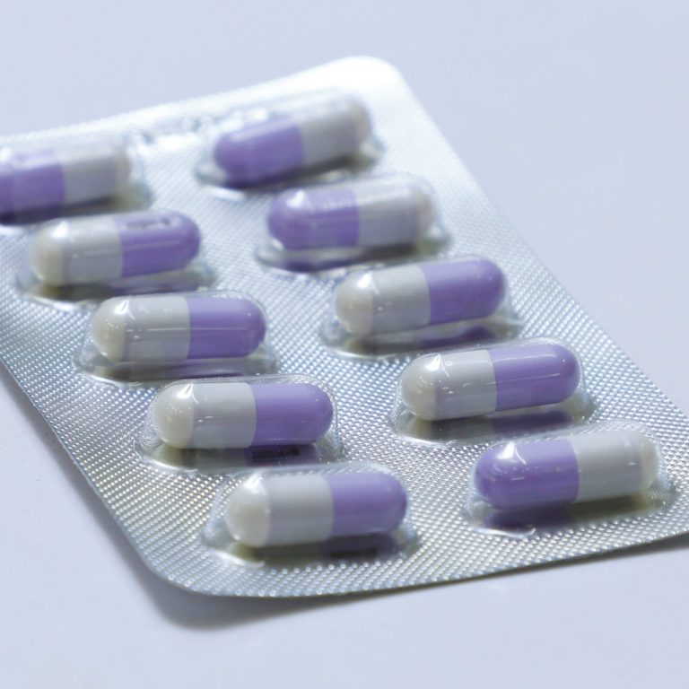 Blisterpack mit lila-weißen Kapseln. Zehn Kapseln in Reihe angeordnet.
