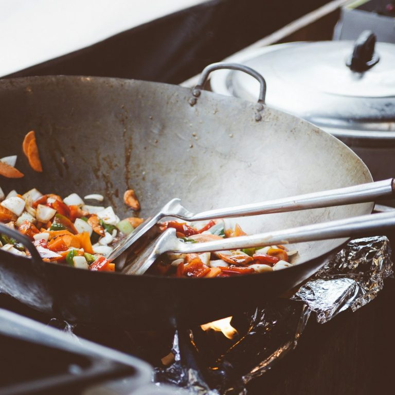 Wok mit buntem Gemüse auf dem Herd, Kochutensilien liegen daneben.