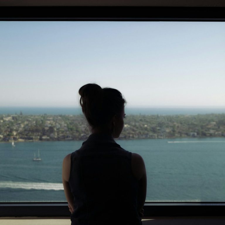 Frau schaut nachdenklich auf das Wasser und die Küstenlandschaft von einer hohen Aussicht.