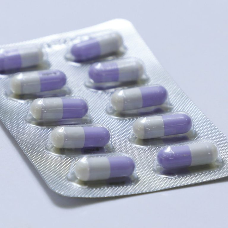 Blisterpack mit lila-weißen Kapseln. Zehn Kapseln in Reihe angeordnet.