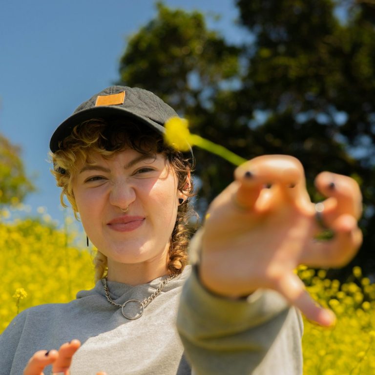 Junge Frau in einem Feld voller Blumen, die eine Blume in der Hand hält und lächelt.